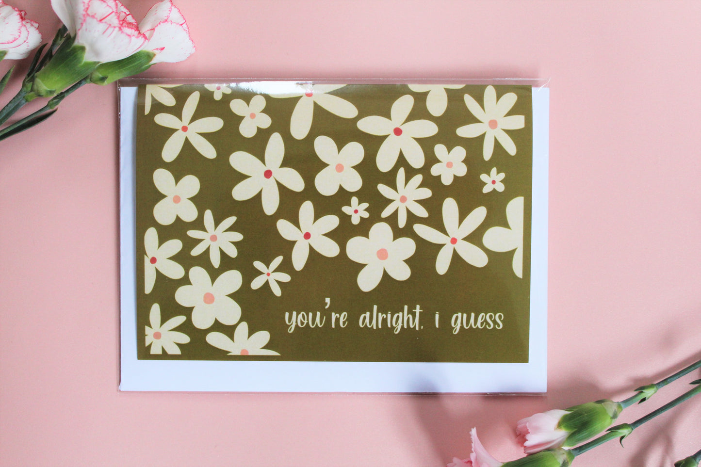 "You're alright, I guess" greetings card, with olive green background and cream coloured flower pattern.