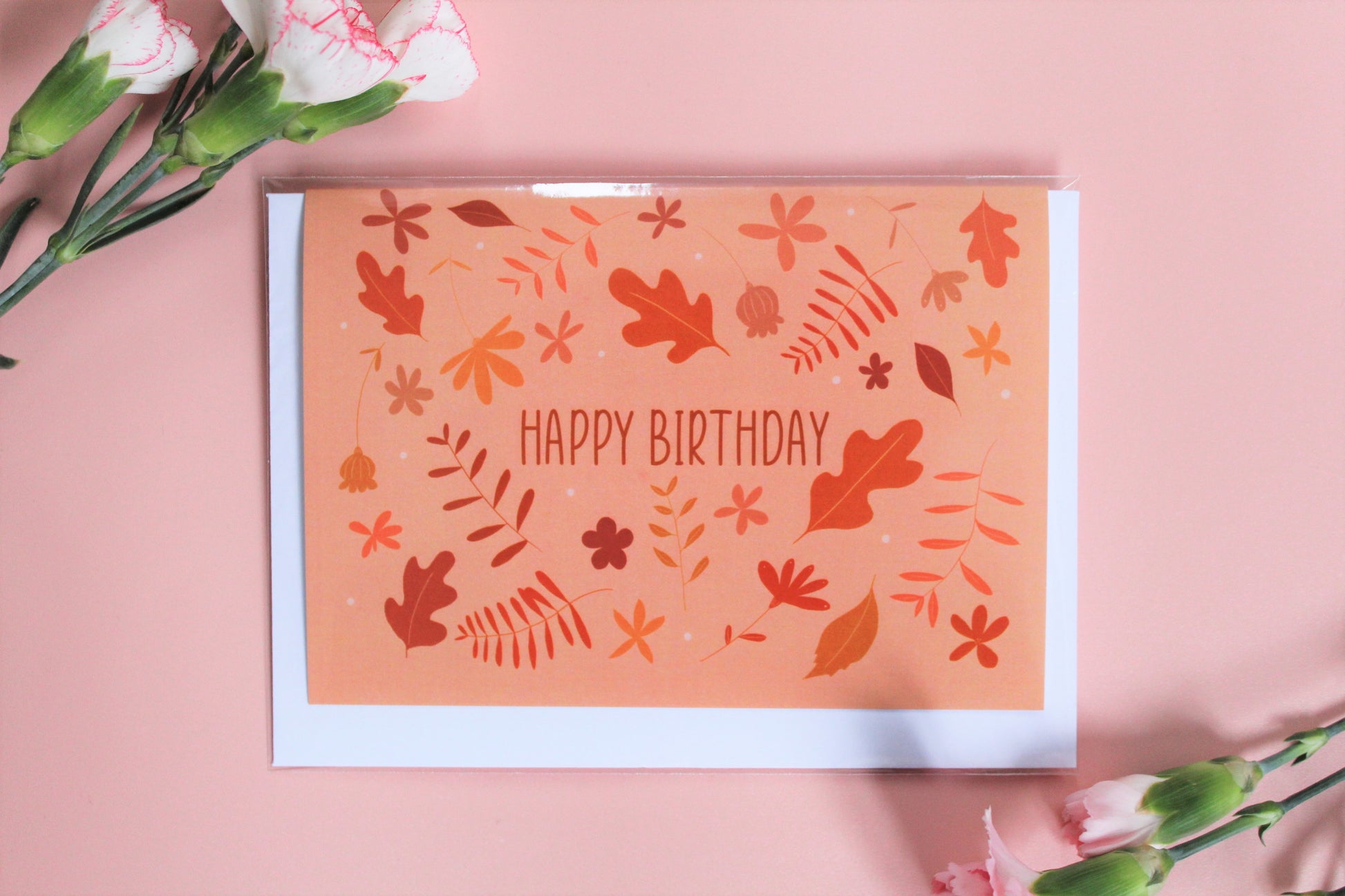 "Happy Birthday" greetings card with peach background with an autumnal colour foliage pattern