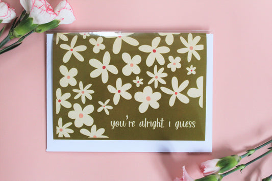 "You're alright, I guess" greetings card, with olive green background and cream coloured flower pattern.